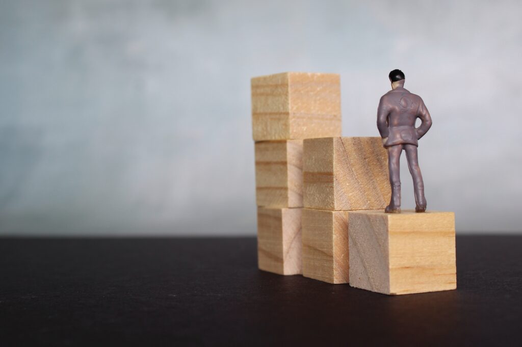 A miniature toy figure stands on a stack of wooden blocks, symbolizing career stability.