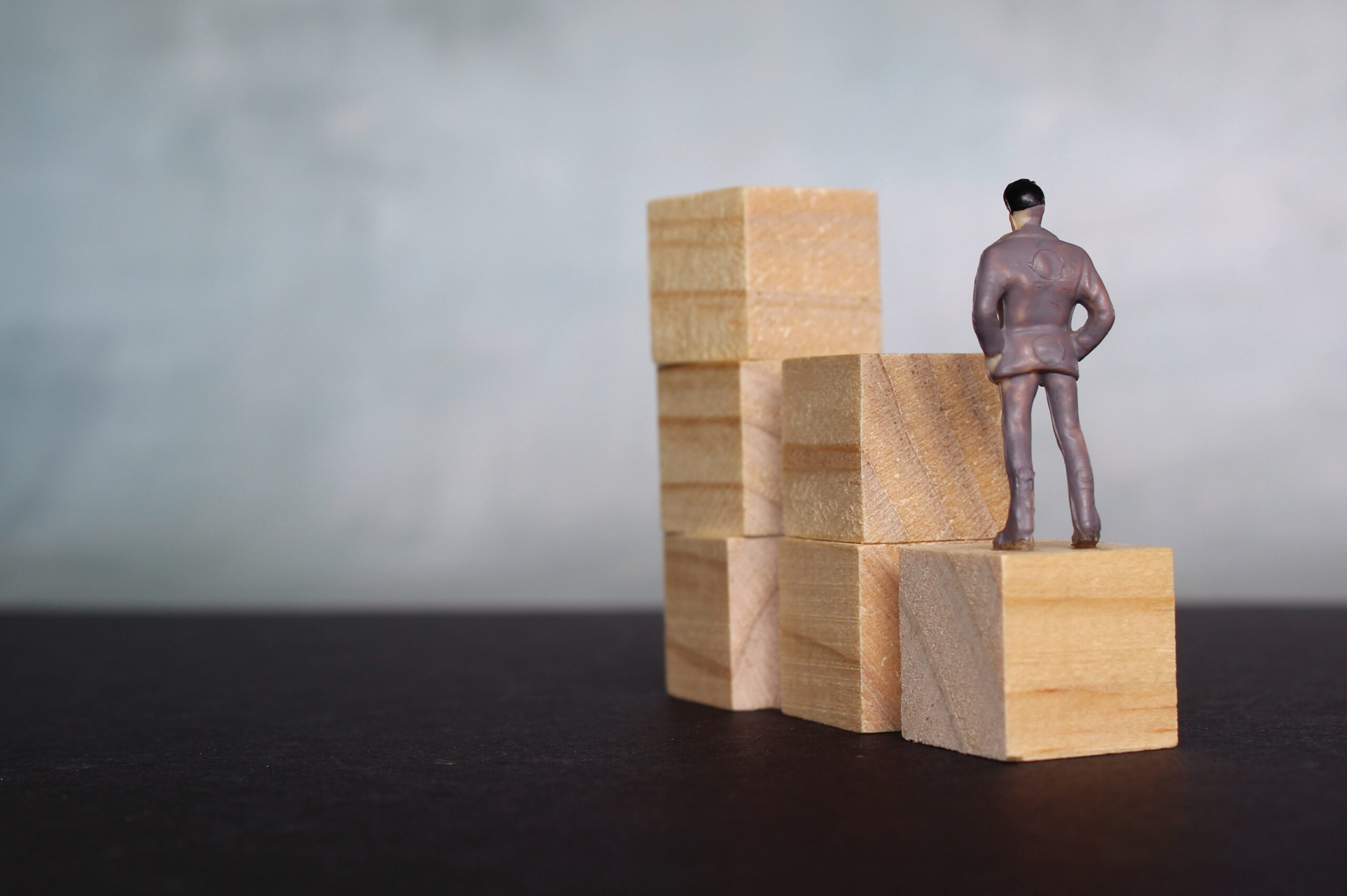 A miniature toy figure stands on a stack of wooden blocks, symbolizing career stability.